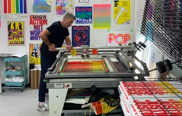 A person in a room decorated with print on the walls and working a press.