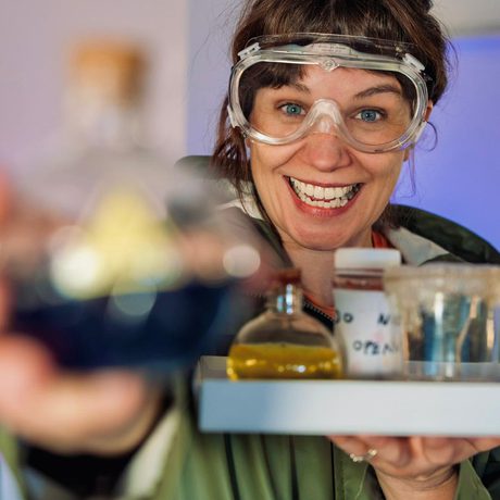 A person wearing protective goggles holding a tray of potions.