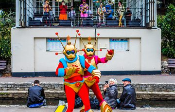 Two alien characters with red and gold outfits, outside in front of band playing on a stage above.