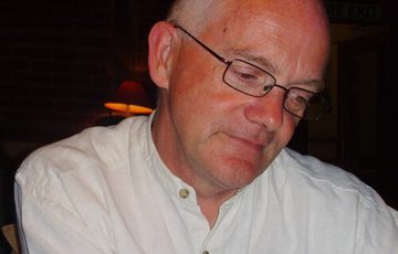 A headshot of a person with glasses wearing a white shirt and is looking down.