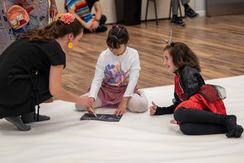 Two children and adult sitting on a the floor, one child is drawing.