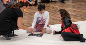 Two children and adult sitting on a the floor, one child is drawing.