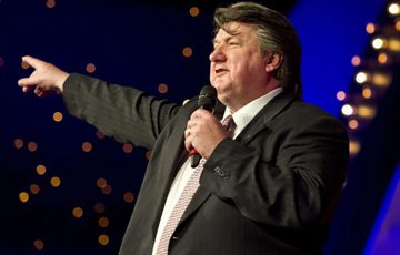 Bob Mills on staging, pointing and holding a microphone.