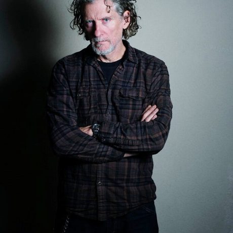 Photograph of a man with his arms crossed standing against a grey background
