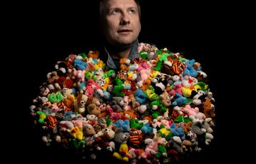 A man wearing a multicoloured top made of small toys against a black background