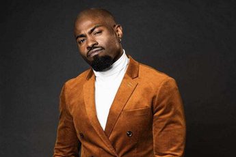 Darren Harriott wearing a brown/orange suit against a black background.