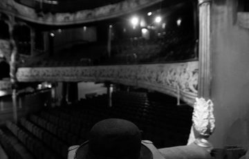 Black and white picture of a leather case and black bowler hat placed on a seat in a theatre