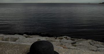 posetr of bowler hat on a sea wall with sea and clouds. Title text in white "The Last Dance of the Cookoos"