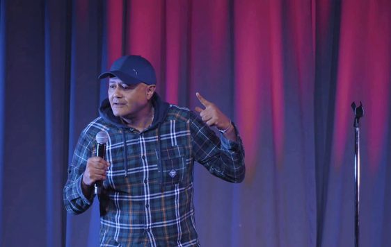Nik Coppin on stage holding a microphone.