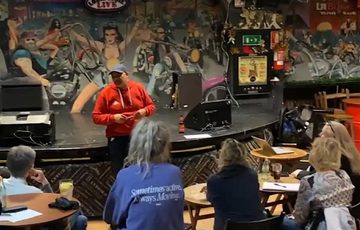 Nik Coppin standing and talking to a small group of people who are sitting at tables.