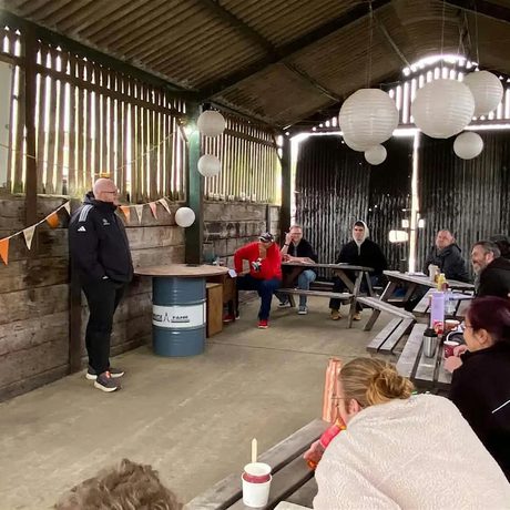 Nik Coppin standing in a decorated barn in front of a group of people sitting at tables.