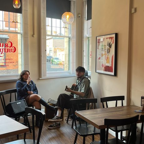 Two adults sitting in a cafe, one is singing while the other is playing a guitar.
