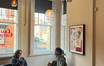 Two adults sitting in a cafe, one is singing while the other is playing a guitar.