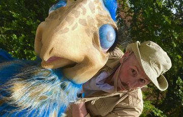 A person is holding on to a blue and cream dinosaur puppet.