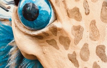 A close up of a blue and cream dinosaur with large blue eye with long eyelashes and giraffe-like spots.