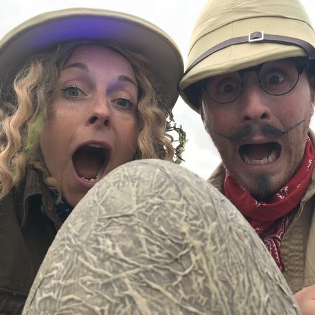 Two people in safari costumes looking an an egg prop with surprised expressions on their faces.