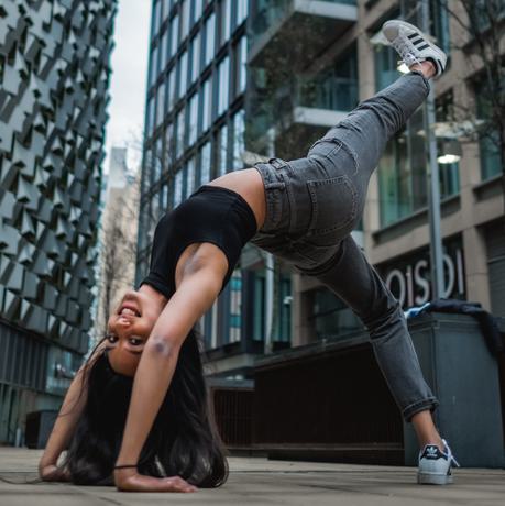 A dance doing a backbend with a leg in the aid. In the background are modern buildings.