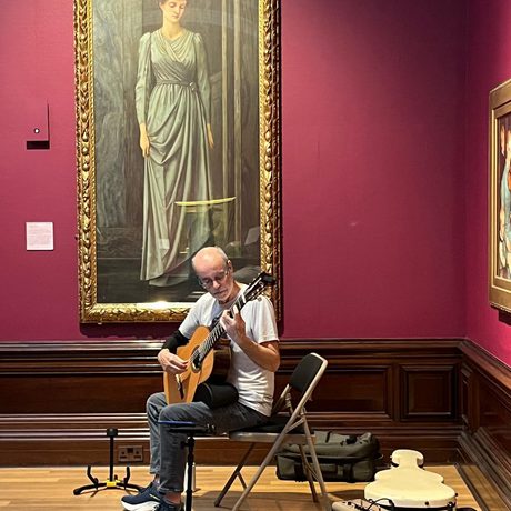 A person playing a guitar in the gallery with paintings in the background.