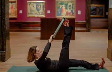 Woman exercising on a mat, stretching leg using a yoga strap in an art gallery.