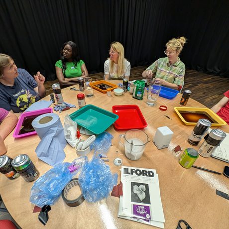 A group of people sitting around a round table with craft supplies on the table.