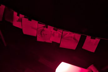A dark photo lit with a red light of paper hanging on a line.