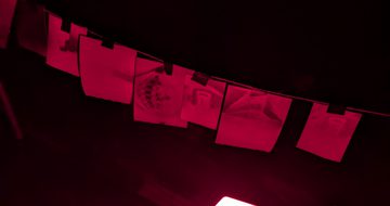 A dark photo lit with a red light of paper hanging on a line.