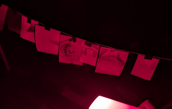 A dark photo lit with a red light of paper hanging on a line.