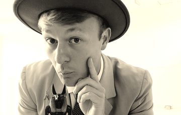 Black and white photo of a person dressed in a suit and hat holding a replica Egyptian statue.