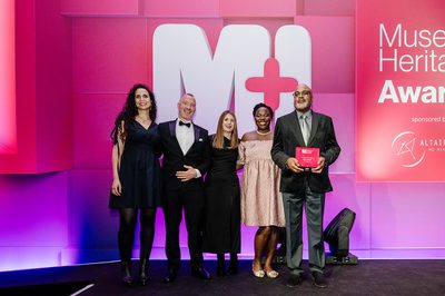 A group of 5 people on a stage one is holding a Museum + Heritage Award.