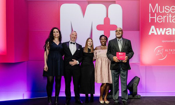 A group of 5 people on a stage one is holding a Museum + Heritage Award.