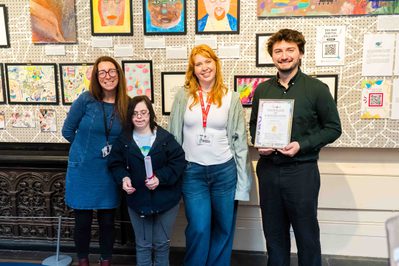 A group of people standing proudly in front of artwork created by Citizens of Midland Mencap.