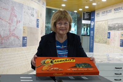 A lady standing an holding a game of Cluedo.