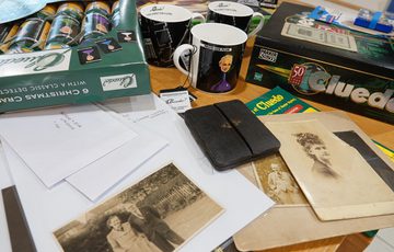 Black and white photos, letters and Cluedo game artefacts on a table.