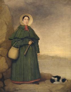 A painting of a lady standing outside, she wears a green dress with bonnet and holds a hammer or tool and carries a basket. She is standing next to a large rock and the sea behind her. A dog is curled up at her feet.