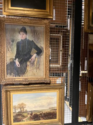 Three paintings in gold frames hanging on a wire storage rack in an archive.