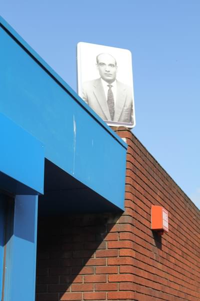 There is a large image on top of a building. The image is in the style of a old black and white passport photo, and shows a man is a suit.