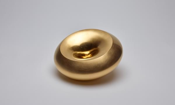 Circular shaped golden coloured vessel with a dip in the middle that makes a small recess.
