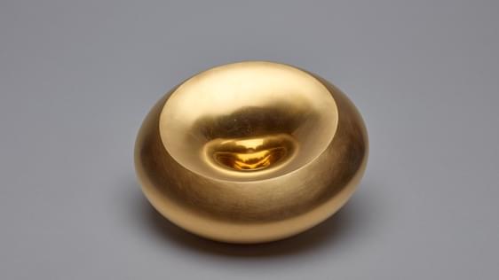 Circular shaped golden coloured vessel with a dip in the middle that makes a small recess.