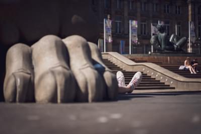 A person's feet can be seen poking out from behind the large foot of a statue.