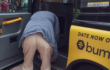 A man is bending over to look into the back of a black taxi. The taxi appears to have the word bum written on it as part of an advert.