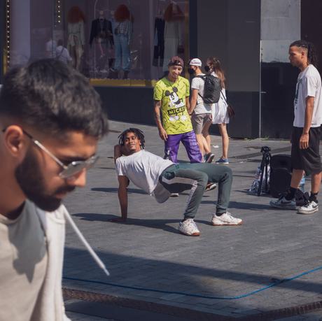 A young man is dancing in the street, as his two friends look on smiling.