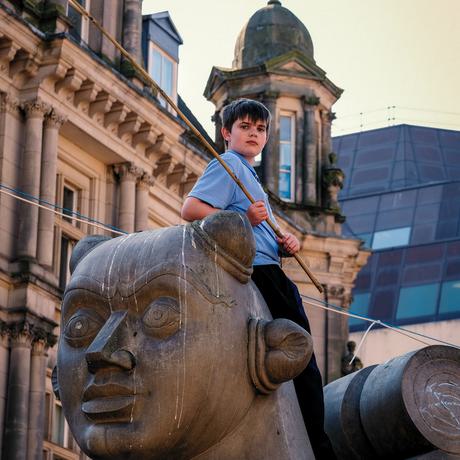 A boy holding a flag is standing on a statue of sphinx. The statue has writing in pink chalk on it's neck that reads: You have the power to change the future.