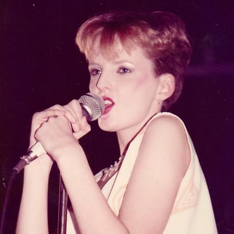 Clare Grogan of Altered Images. She's singing into a mic, has short hair and a white top. She's got bright red lipstick