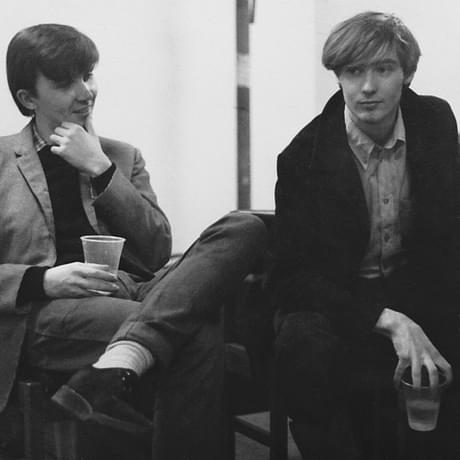Campbell Owens and Roddy Frame of Aztec Camera. They're both young men and look well groomed with floppy hair and blazers. Both are holding a drink in plastic cups