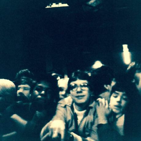 A packed crowed all pushed to the front. People reach over the barrier. Everyone looks happy, but hot and sweaty