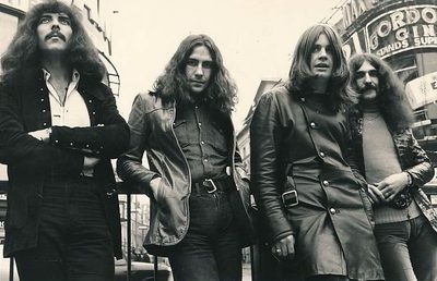 A black and white photo of the members of Black Sabbath standing outside in 1970.