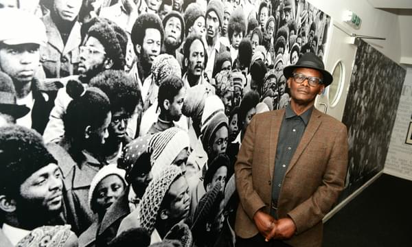 Vanley Burke stands in front of an image from one of his photographs that has been blown up to be very large in size.