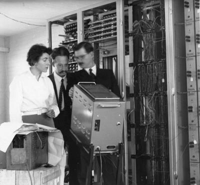 Black and white photo of a lady and two men alongside computer machinery.