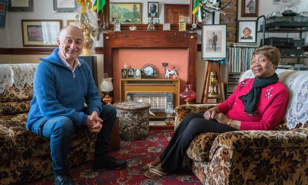 Presenter Tony Robinson is sitting in a living room with Mavis. The room is full of photos and ornaments.