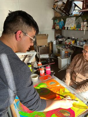 A person painting a colourful artwork while another looks on.